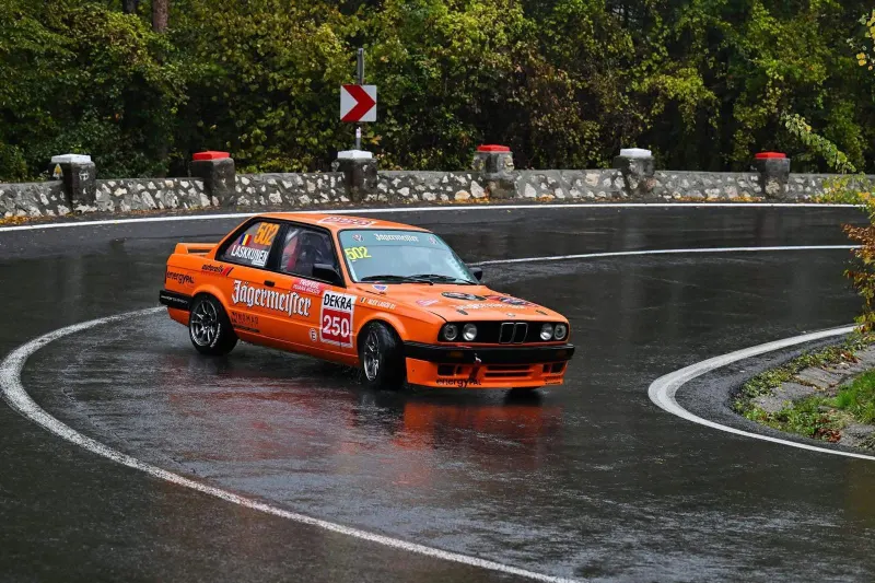 Orange BMW E30 race car cornering on a wet mountain road